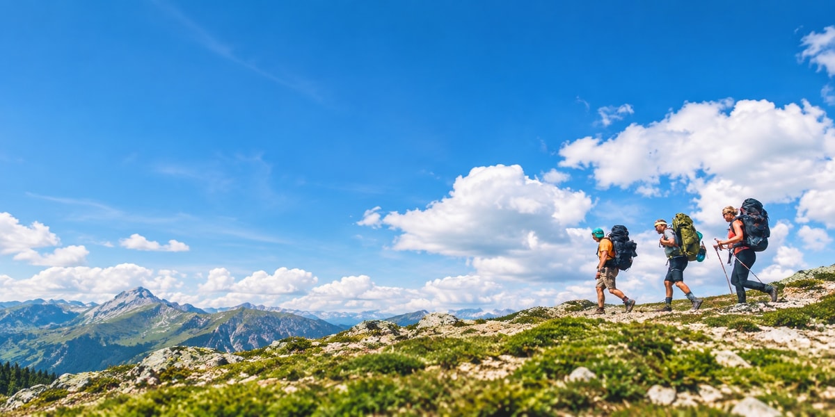 Three people hiking along a mountain ridge under a blue sky