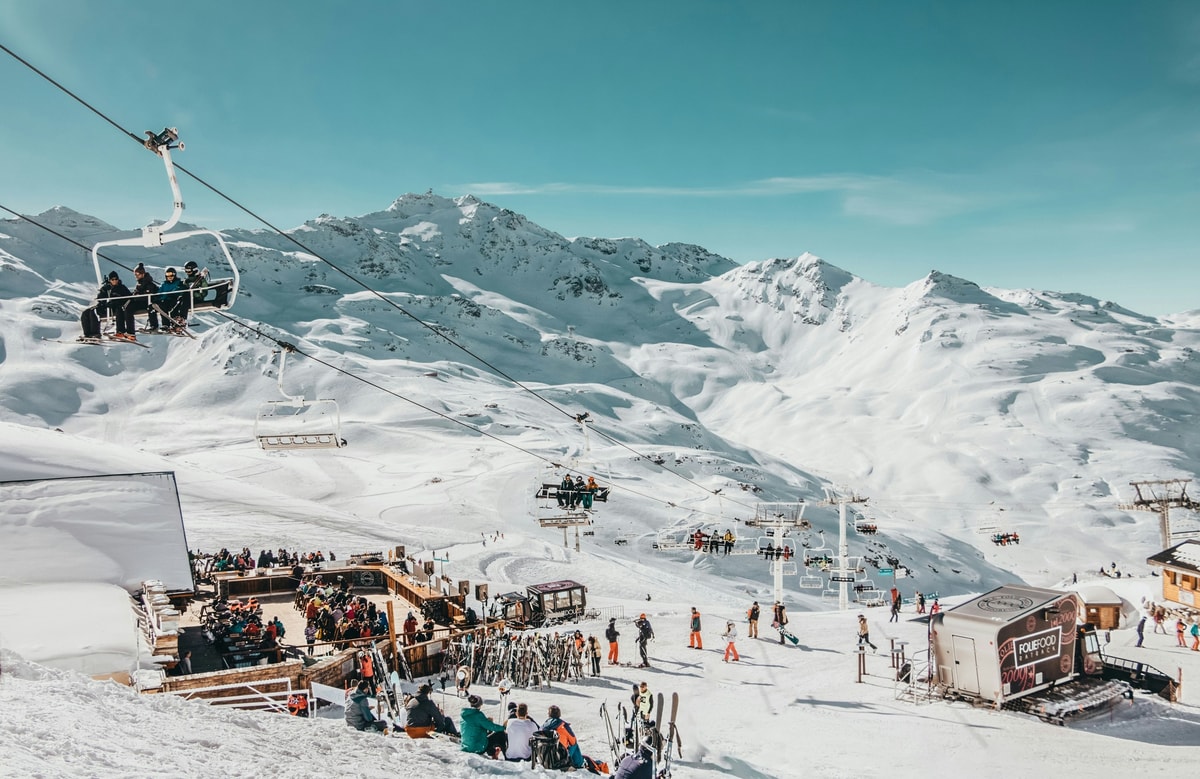 Val Thorens village in a snowy bowl below white peaks, with a chairlift carrying skiers up the slope in front