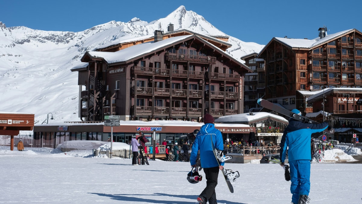 Two skiers walking past chalet-style hotels at the foot of the slopes in Tignes